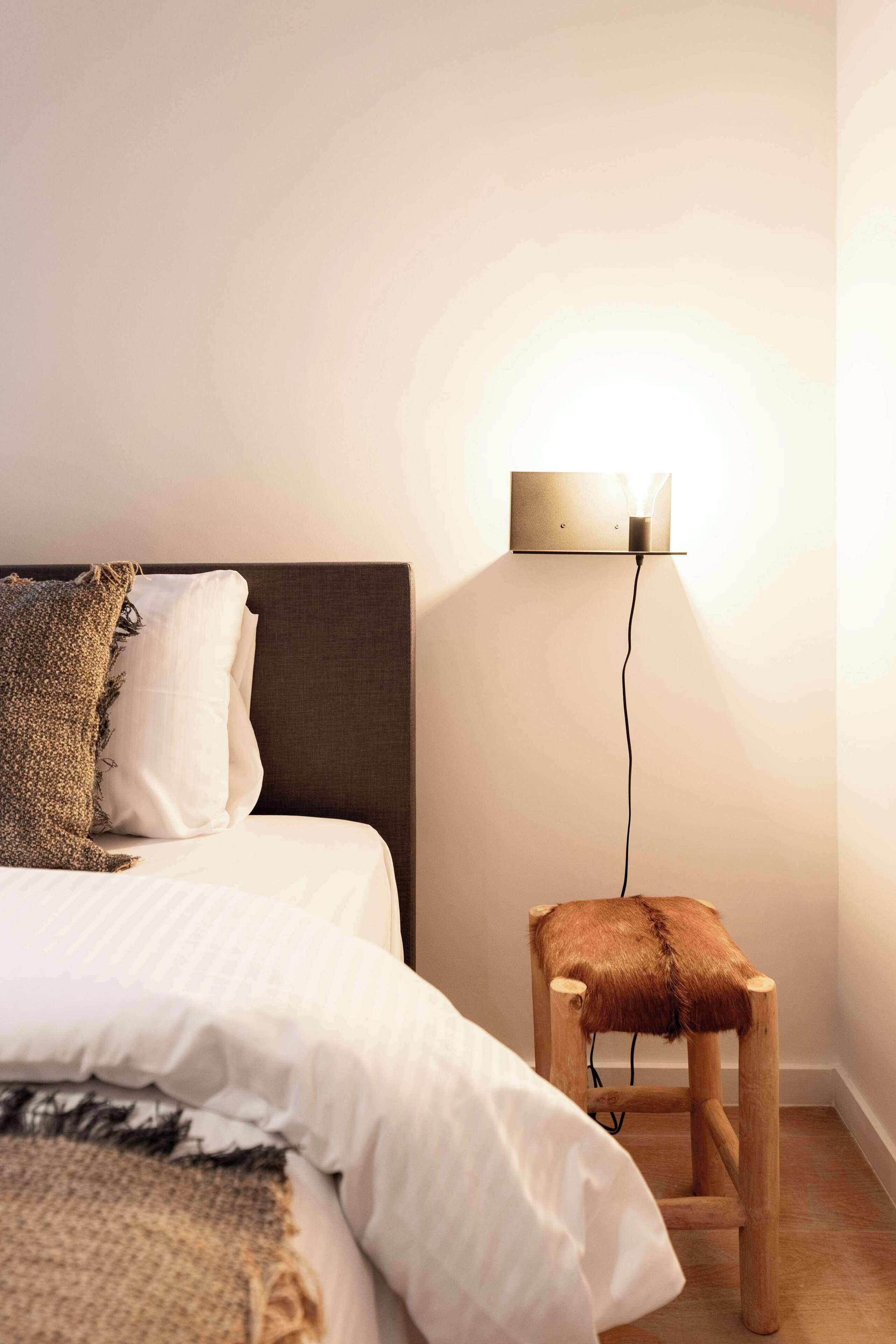 Un dormitorio con una cama, una mesita de noche y un aplique de pared.