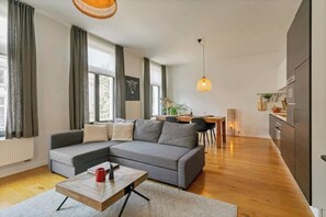 Un salon moderne avec un canapé d’angle gris, une table basse en bois et un coin repas comprenant une table et des chaises en bois.