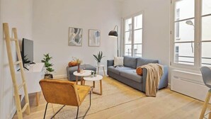 A modern living room with a sofa, coffee table, and a desk. There are plants, a ladder, and a large window providing natural light. - Chic 1-BR in Antwerp's Center (Antwerpen)