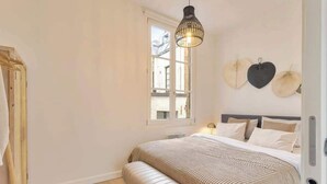 A bedroom with a large bed, a bench, a hanging light fixture, and a window with a view. - Chic 1-BR in Antwerp's Center (Antwerpen)