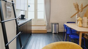 A compact kitchen with a sink, stove, and cabinets. There's a dining area with a table and chairs, and a trash can. - Spacious Triplex Apartment in Mechelen (Mechelen)