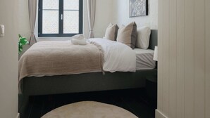 A neatly arranged bedroom with a bed, pillows, a bedside table, and a window with curtains. - Spacious Triplex Apartment in Mechelen (Mechelen)