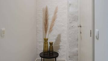 A narrow hallway with white walls and a black floor. There is a small round table with two vases containing pampas grass.