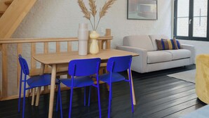 A modern living room with a wooden dining table, blue chairs, a white sofa with patterned cushions, and a large window with a view of a brick building. - Spacious Triplex Apartment in Mechelen (Mechelen)