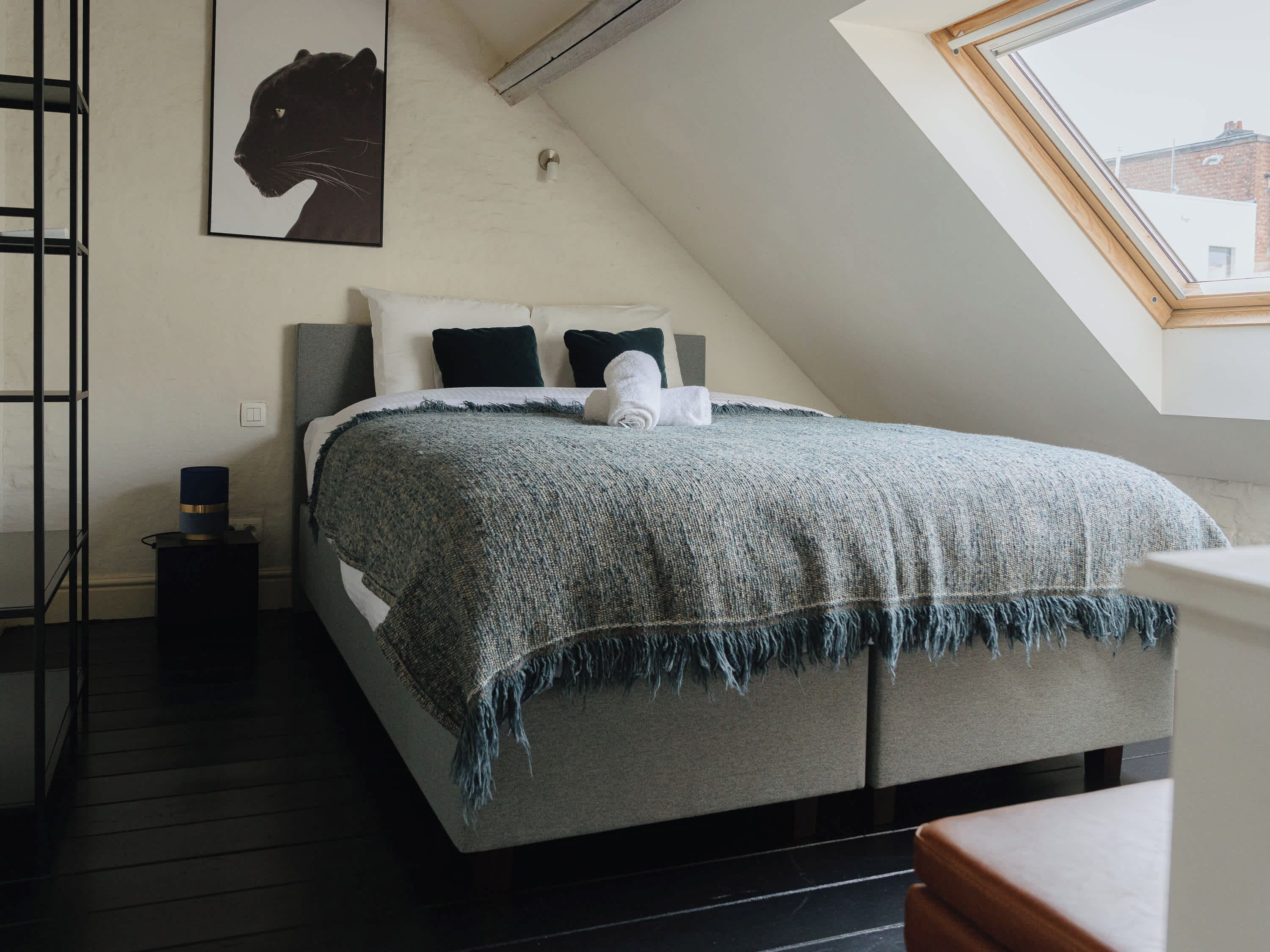 A bedroom with a loft-style ceiling, a bed with a grey blanket, a black and white poster on the wall, and a skylight.