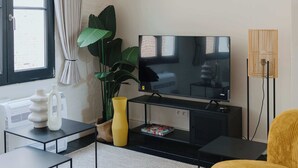 A modern living room with a flat-screen TV, a yellow armchair, a coffee table, a plant, and a floor lamp. - Spacious Triplex Apartment in Mechelen (Mechelen)