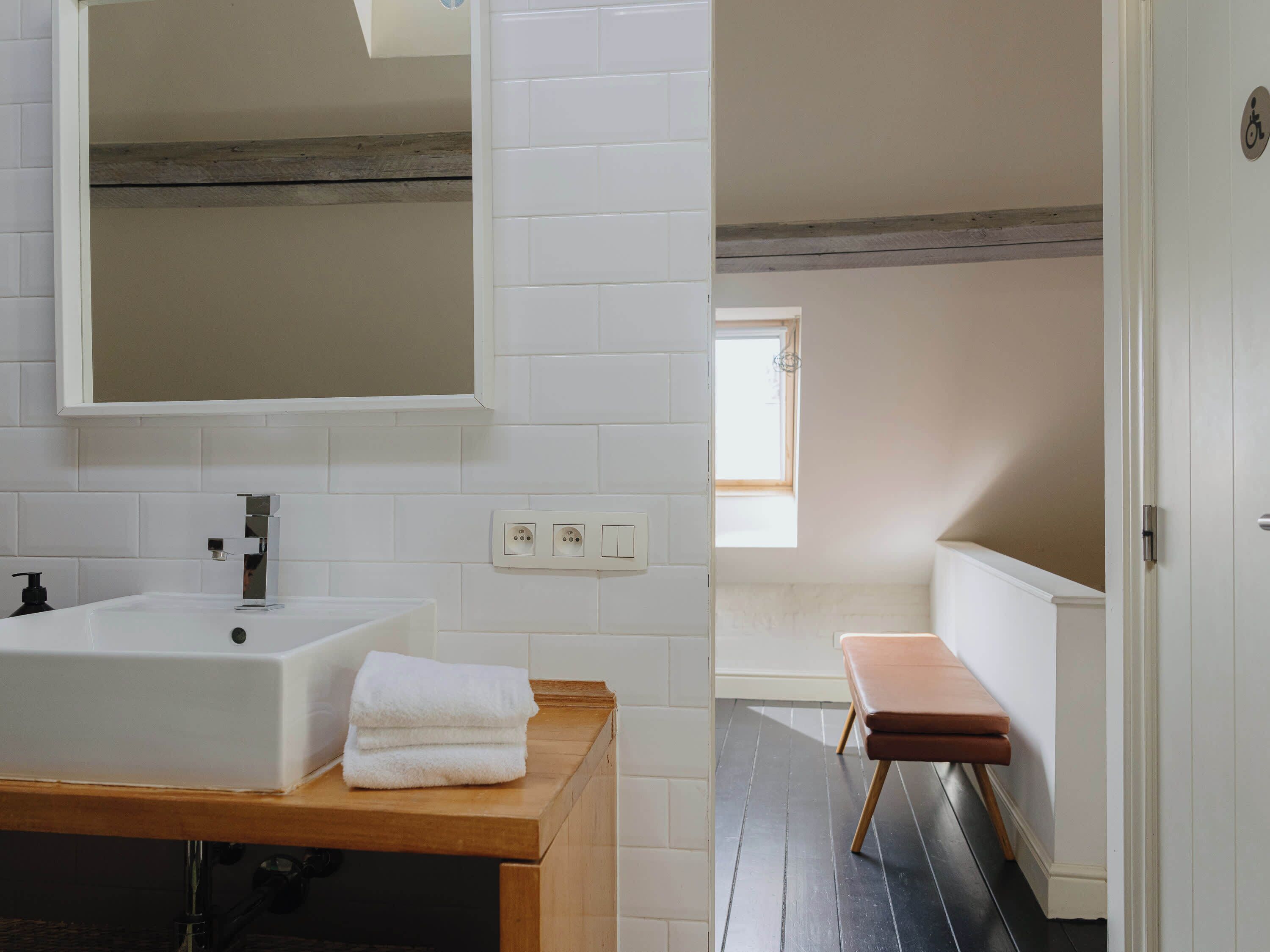Une salle de bain moderne avec un lavabo blanc, un miroir et un banc en bois.