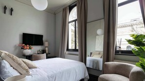 Et moderne hotelværelse med en stor seng, to lænestole, et fladskærms-tv og et stort vindue med gardiner.