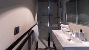 Et moderne badeværelse med et brusekabine i glas, en hvid vask med marmorbordplade og et stort spejl.