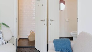 A room with a white door leading to a bathroom with a white toilet and a mirror. There is a wicker basket on the floor near the door.
