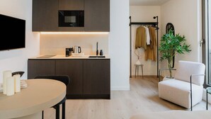 A modern kitchen with a built-in microwave, a coffee maker, and a kettle on the counter. There is a dining table with chairs and a small potted plant. - Elegant and Spacious Suites (Antwerpen)