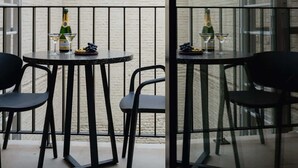 Una piccola area pranzo all'aperto con due tavoli e sedie, una bottiglia di champagne e un bicchiere su un tavolo.