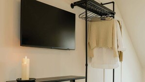 A modern room with a flat-screen TV mounted on the wall, a black console table with a candle, a white ottoman, and a black drying rack with clothes. - Spacious Suite for 4 with Kitchenette (Antwerpen)