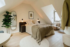 A modern bedroom with a sloped ceiling, a bed with a beige blanket, a bedside table with a lamp, a large mirror, and a potted plant. - Spacious Suite for 4 with Kitchenette (Antwerpen)