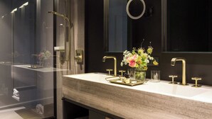Een moderne badkamer met een grote spiegel, twee gouden kranen en een houten wastafelmeubel.