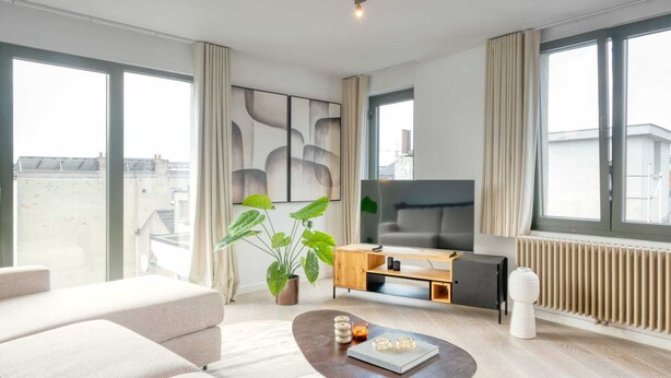 Ein modernes Wohnzimmer mit einer Couch, einem Couchtisch, einem Fernseher und einer Zimmerpflanze.