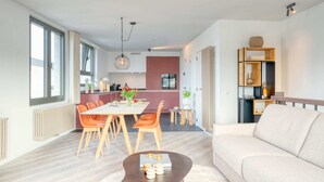 Ein modernes Wohnzimmer mit einer Couch, einem Essbereich mit Tisch und Stühlen sowie einer Küche im Hintergrund.