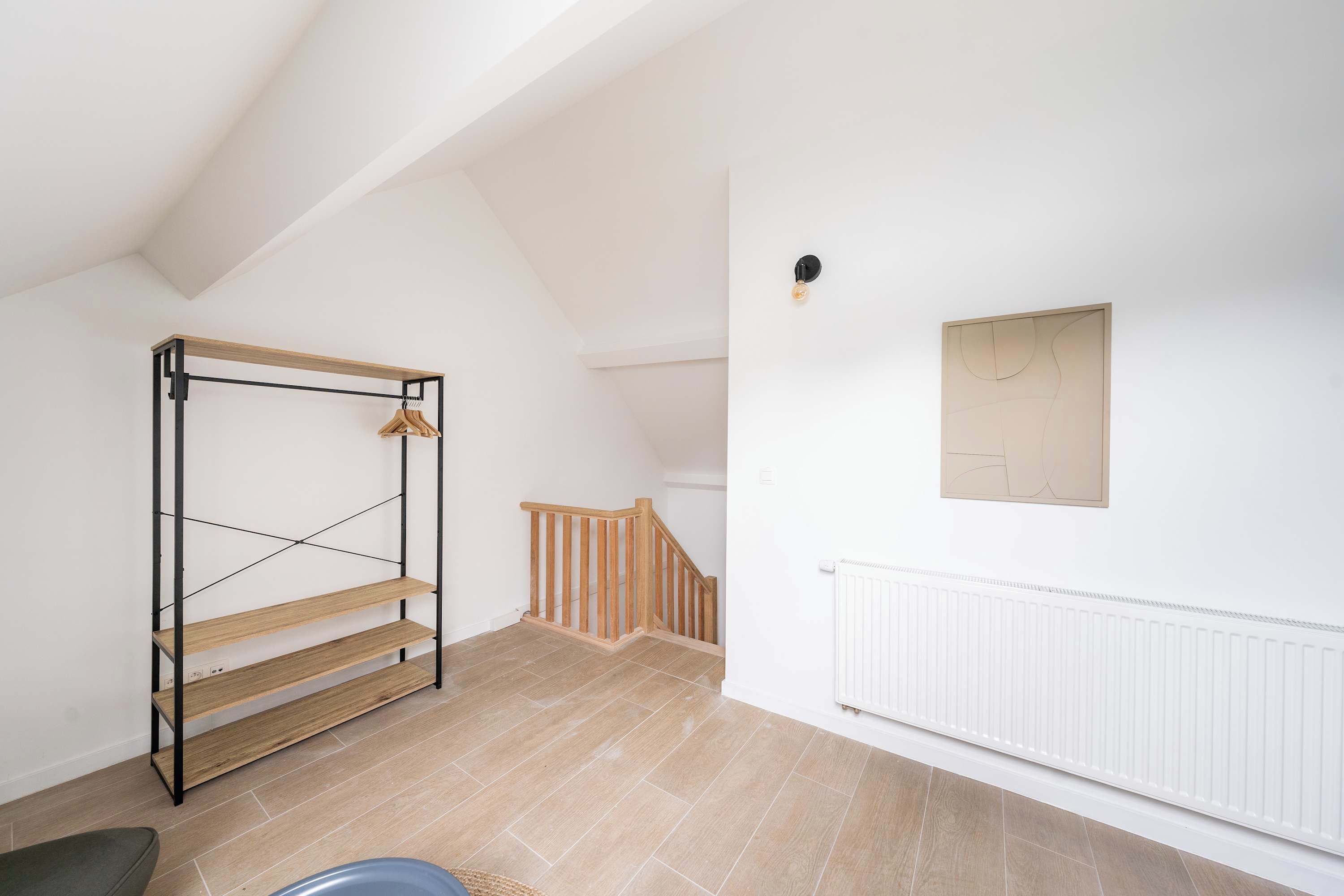 A room with a wooden shelf unit, a white radiator, and a staircase with wooden railings.