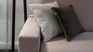 Ett modernt vardagsrum med en golvlampa, en soffa med kuddar och en inramad svartvit målning som föreställer en stadsbild, hängd på väggen.