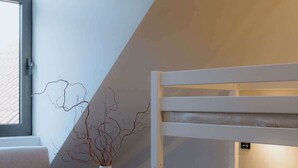 Un dormitorio moderno y funcional con una cama litera, una pequeña mesa redonda con un florero, un sofá y un amplio ventanal.