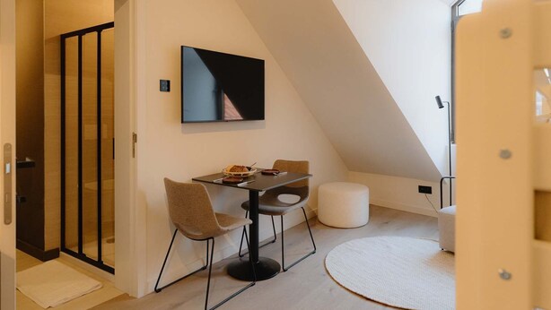 Una habitación moderna y compacta con una mesa de comedor y sillas, un televisor de pantalla plana montado en la pared y una alfombra redonda pequeña.