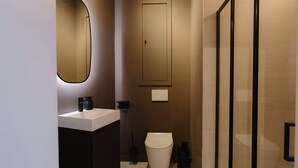 Un baño moderno con un lavamanos blanco, un espejo, un inodoro y una zona de ducha.