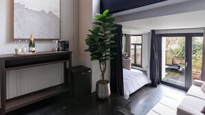 Una camera d'albergo moderna con una grande finestra, una pianta in vaso, un minibar e un letto con vista sul giardino.