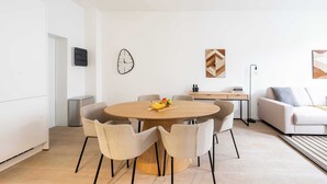 Un saló modern amb una taula rodona de fusta per dinar envoltat de sis cadires, un sofà i una taula de centre amb fruita.