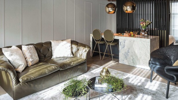 Un salon moderne avec un canapé en cuir, une table basse en marbre et un coin bar équipé de tabourets.