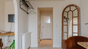 A hallway with a wooden floor, a white door at the end, a radiator, a hanging clothes rack, and a mirror with a wooden frame. - Cozy Hideaway Near the Heart of Antwerp (Antwerpen)