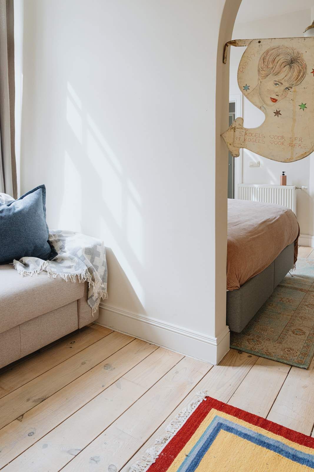 A cozy room with a sofa, a bed, a patterned rug, and a wall with a unique artwork.