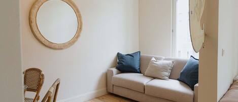A room with a beige sofa, a round mirror, a wicker chair, and a colorful rug.