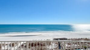Vista de la playa desde un balcón con barandilla, océano y cielo despejado.
