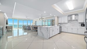 Una cocina moderna con una isla grande, muebles blancos y vistas al océano.