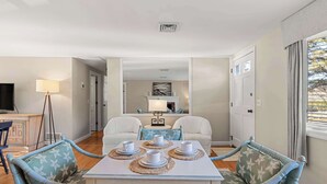 En spiseplads med et bord dækket til fire personer, en sofa og et fjernsyn i baggrunden.