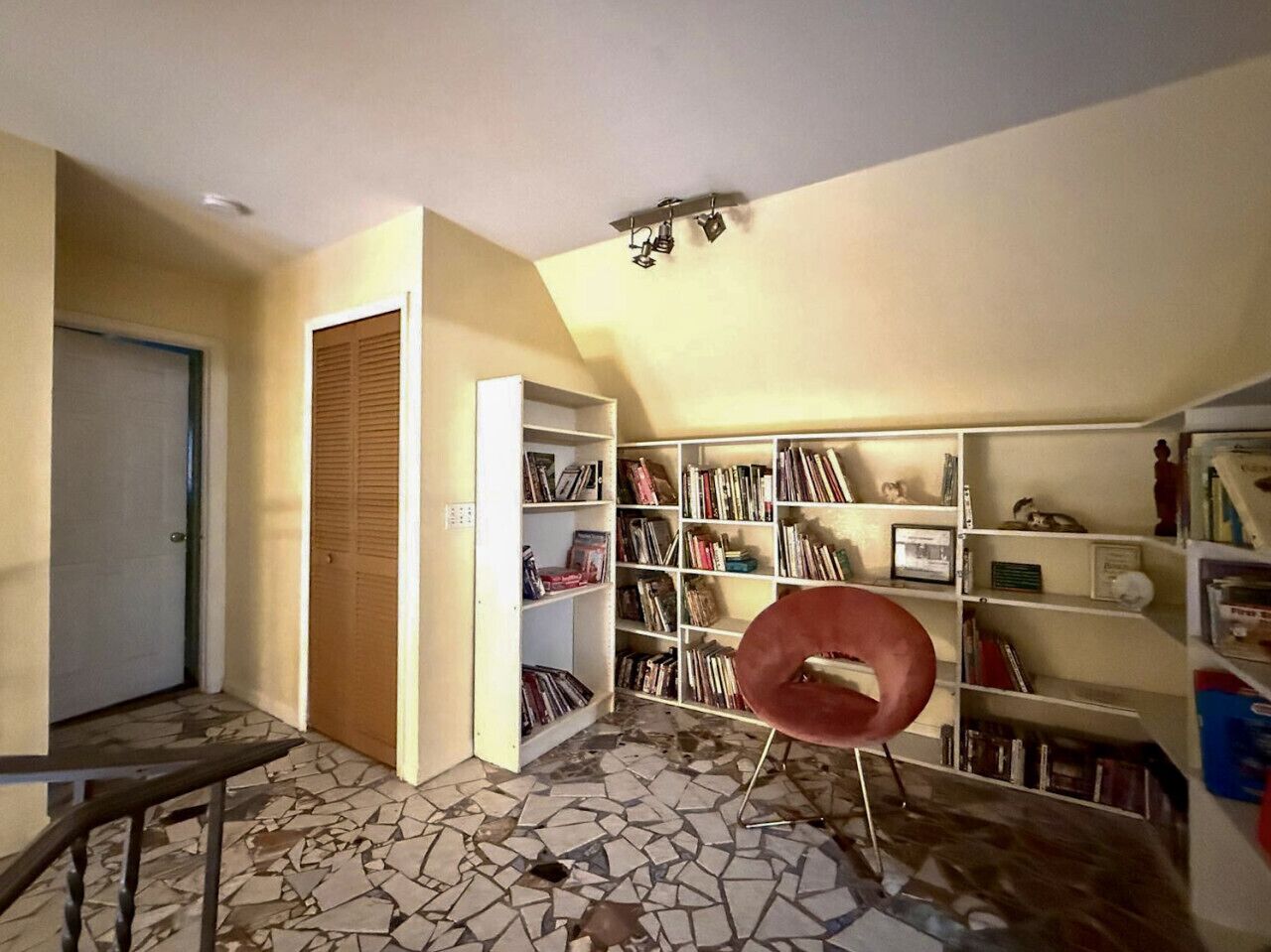 A room with a tiled floor, a bookshelf, a wooden door, and a red chair.