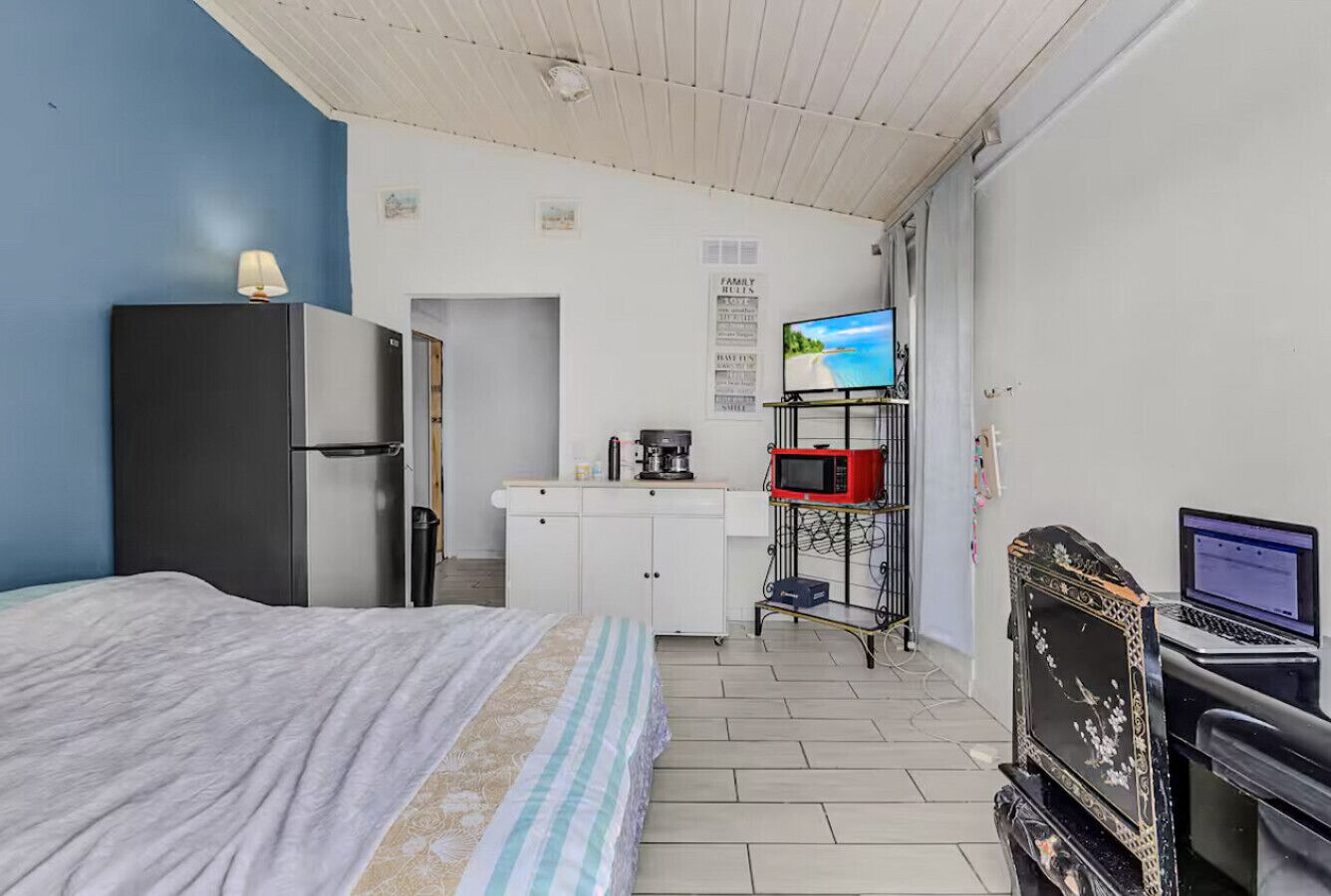 A bedroom with a bed, a desk with a laptop, a microwave, and a TV.
