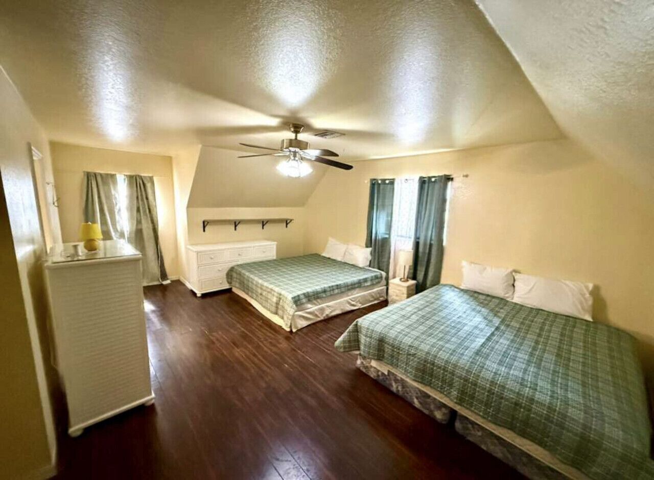 Une chambre avec deux lits, un ventilateur de plafond, un radiateur et une commode.