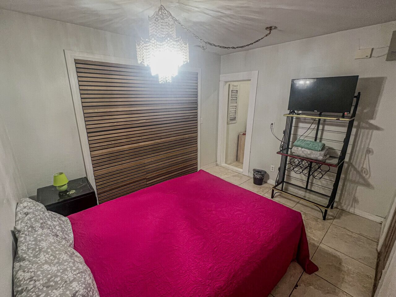 A bedroom with a bed, a bedside table, a TV stand, and a door.