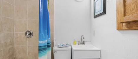 Un baño con ducha, inodoro, lavabo y un mueble pequeño.