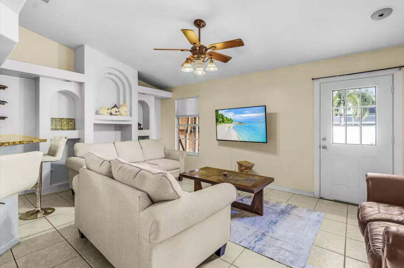 A living room with a beige sofa, a coffee table, a TV, and a ceiling fan.