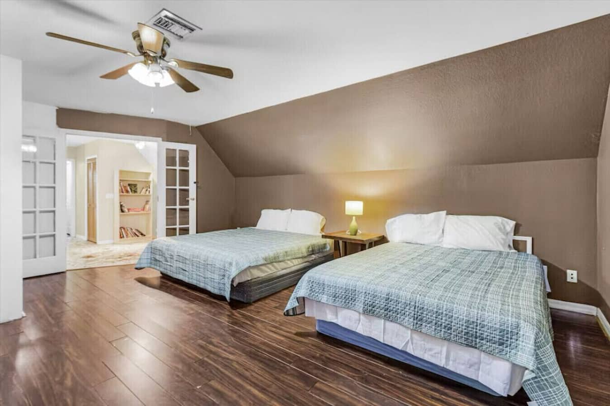Ein Schlafzimmer mit zwei Betten, einem Deckenventilator, einem Nachttisch mit Lampe und einem Bücherregal.
