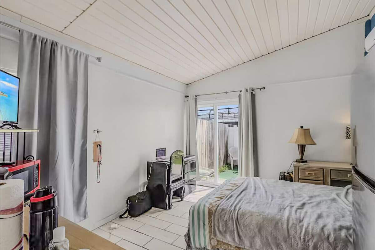 Ein Hotelzimmer mit einem Bett, einem Schreibtisch mit Computer, einem Telefon, einer Lampe und Blick ins Freie.