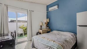 Hotellihuone, jossa on sänky, työpöytä, tuoli, yöpöytä, lamppu ja ilmastointilaite.