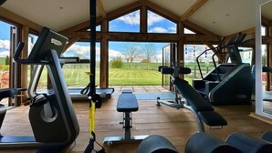 Een sportschool met trainingsapparatuur, grote ramen en uitzicht op het omliggende landschap.