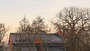 Een stenen gebouw met schuine kap, omgeven door bomen en een haag.