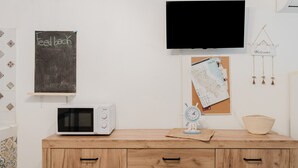 Ein Zimmer mit einem Holzkasten, einer Mikrowelle, einem Korkbrett mit Papieren, einer Uhr und einem an der Wand befestigten Fernseher.