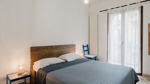 Ein Schlafzimmer mit Bett, Nachttisch, Stuhl und einem Fenster mit Vorhängen.