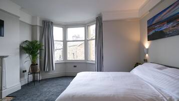 A hotel room with a large bed, a potted plant, a view of buildings through the window, and a painting on the wall.