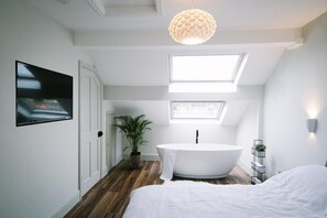 A modern bedroom with a large bed, a white bathtub, a potted plant, and a ceiling light fixture. - Ashfield (Lancaster)